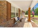 Inviting front porch with wooden flooring, brick columns, and comfortable seating with an American flag at 2079 Leguin Mill Rd, Locust Grove, GA 30248