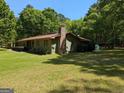 View of home exterior with green siding and brick chimney surrounded by mature trees and a lush lawn at 1710 Crumbley Rd, Mcdonough, GA 30252