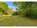 View of the front yard and exterior of the red home surrounded by mature trees and landscaping at 362 Highway 113, Temple, GA 30179