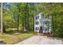 Side view of three-story home with white siding, black shutters surrounded by lush, mature trees and long driveway at 4448 Janice Dr, Snellville, GA 30039
