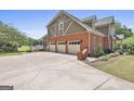 View of the three-car garage with red brick and gray trim, plus a large driveway at 780 Birkdale Dr, Fayetteville, GA 30215