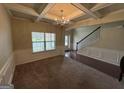 Spacious living room featuring a coffered ceiling, elegant chandelier, and stylish wainscoting, seamlessly blending carpet and hardwood flooring at 960 Spanish Moss Trl, Loganville, GA 30052