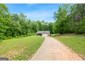 A single-story home sits on a large lawn with a long driveway and is surrounded by abundant trees and greenery at 3775 Highway 16 E, Sharpsburg, GA 30277