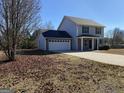 Two story home featuring a two-car garage, vinyl siding, and a spacious front yard during the winter at 253 Whistle Way, Locust Grove, GA 30248