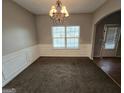A dining room illuminated by a chandelier, wainscoting, neutral walls, a large window and an arched doorway at 6206 Flat Trace, South Fulton, GA 30291