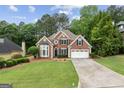 Traditional brick home featuring a lush lawn, mature trees, and a two-car garage at 7020 Grand View Way, Suwanee, GA 30024