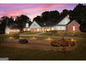 Elegant home with a brick facade, lush landscaping, and warm exterior lighting against a vibrant sunset sky at 228 Indian Creek Rd, Locust Grove, GA 30248