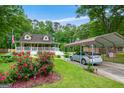 View of the home and carport from the yard, showcasing lush landscaping and beautiful red rose bushes at 3777 Edward Rd, Rex, GA 30273