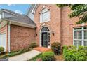 Close up of a brick home's arched doorway with black door, flanked by green shrubs and manicured landscaping at 232 Spalding Gates Drive, Atlanta, GA 30328