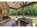 Covered outdoor patio boasting a stone fireplace, wooden beams, and a view of the private backyard at 71 Pacific Ave, Sharpsburg, GA 30277