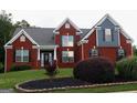 Red brick home with black shutters and a well-manicured lawn featuring landscaping and mature trees at 141 Windward Hills, Mcdonough, GA 30253