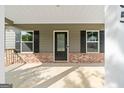 View of the covered front porch showcasing brick accents, a dark front door, and matching window shutters at 385 Orchard Land, Covington, GA 30014