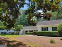 View of the charming one-story home framed with mature tree branches and lush green foliage at 7640 Ryefield Dr, Sandy Springs, GA 30350