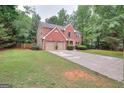 Two-story brick home showcasing a lush green lawn, a long driveway and mature trees creating a private setting at 5765 Woodstone Dr, Cumming, GA 30028