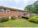 Brick home with wooden deck and stairs, surrounded by green lawn and mature trees at 5141 Hiram Lithia Springs Rd, Powder Springs, GA 30127