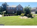 Charming two-story brick home with lush green lawn, mature trees, and colorful flower beds at 1869 Schofield Dr, Hampton, GA 30228