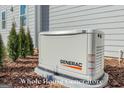 Whole house Generac generator is wired to the house and sits beside some small evergreens at 915 Laurel Brooke Ave, Peachtree City, GA 30269