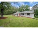 Lovely ranch style home with white brick, dark shutters, a red door, and a sprawling green lawn at 3290 Ebenezer Se Rd, Conyers, GA 30094