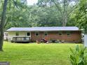 View of the back of a brick home with a lawn, deck, and mature trees, providing a private outdoor space at 3683 Miller St, Lithia Springs, GA 30122