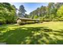 Sprawling backyard view of brick ranch home nestled among mature trees with lush, green lawn at 160 Pine Trail Rd, Fayetteville, GA 30214