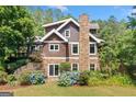 Rear exterior of the home featuring wood siding, stone accents, a stone chimney, and landscaped garden beds at 99 Landers Ne Rd, Rydal, GA 30171