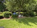 Lush backyard garden featuring shade trees, blue flowers, manicured hedges, and a quaint seating area at 404 Windsor Way, Peachtree City, GA 30269