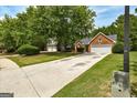 Residential street view of a one-story brick home with two-car garage, spacious front yard, and mature shade trees at 2504 Plymouth Way, Conyers, GA 30013