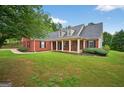 Charming red brick house boasts a covered front porch, classic shutters, and lush green lawn creating a warm, inviting curb appeal at 65 Pecan Ln, Oxford, GA 30054