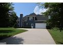 Long concrete driveway leads to a two-car garage, surrounded by a lush green lawn and mature trees at 9 Warrior Way, Sharpsburg, GA 30277
