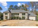 Imposing stone home featuring mature landscaping, a gray shingle roof, and sophisticated modern windows at 825 Kenry Ct, Atlanta, GA 30342