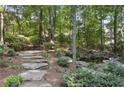 Serene backyard oasis with stone steps leading to a tranquil pond surrounded by lush greenery and mature trees at 1400 Lamont Cir, Dacula, GA 30019