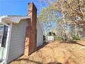 Exterior side view of the house featuring a brick chimney with a spacious wooded lot at 1330 Hillcrest Dr, Sugar Hill, GA 30518