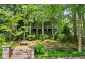 Landscaped front yard with stone steps leading to a charming home nestled among lush trees at 9032 Selborne Ln, Chattahoochee Hills, GA 30268