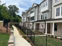 Sidewalk view of modern townhomes featuring manicured lawns and black metal fences on a sunny day at 1980 Flying Scotsman Dr # 10, Kennesaw, GA 30144