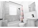 Bright bathroom featuring a white sink, toilet, and bathtub with gray tiled walls and a shower with patterned curtain at 1830 W Taylor Ave, Atlanta, GA 30344