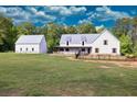 View of white farmhouse-style home with metal roof, detached garage, black fence, and expansive green lawn at 2731 Tribble Mill Rd, Lawrenceville, GA 30045
