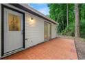 Exterior shot of a white home with a brick patio and a door and sliding glass door, with forest behind at 1428 Muirfield Dr, Stone Mountain, GA 30088