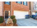 Exterior view of brick townhome with a two car garage, black door, landscaping, and trash cans out front at 1605 Signal Flag Way, Lawrenceville, GA 30043