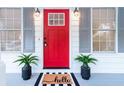 Inviting red front door with black hardware, flanked by potted plants and a stylish welcome mat at 185 Bob White Dr, Stockbridge, GA 30281