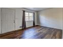 Bright living room featuring new wood-look flooring, a large window with dark curtains, and a white front door at 5990 Mallory Rd, South Fulton, GA 30349