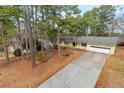 Wide driveway leading to a yellow ranch-style home with attached garage, surrounded by pine trees and natural landscape at 2142 Graystone Pkwy, Grayson, GA 30017