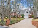 Traditional brick home featuring a manicured lawn, mature trees, and a long driveway to the attached garage at 2055 Pearwood Path, Roswell, GA 30076