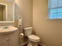 A half bathroom features a sink with a white cabinet, toilet, and window for natural light at 46 Darbys Crossing Ct, Hiram, GA 30141