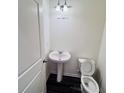 Pedestal sink and elongated toilet in a half bathroom with dark wood-look flooring at 7722 Sudbury Cir, Covington, GA 30014