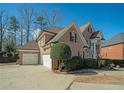 Spacious three-car garage with a brick exterior, a large driveway, and mature landscaping at 6195 Mountainwell Dr, Roswell, GA 30075