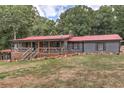 Beautiful gray house with red metal roof, front porch with wooden railings and landscaped yard surrounded by mature trees at 616 Rich Davis Rd, Hiram, GA 30141