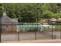 Tennis court with black fencing, lights, and view of the community pool behind the trees at 200 Brookwood Xing, Douglasville, GA 30134