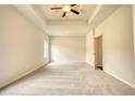 Spacious bedroom with plush carpeting, a tray ceiling, ceiling fan, and ample natural light at 700 Park Place Way, Social Circle, GA 30025