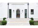Elegant home entrance featuring a modern arched door, complemented by stone steps and manicured bushes at 100 Tuxedo Nw Ter, Atlanta, GA 30342