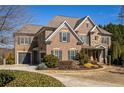 Two-story brick home boasts a stone accent, an attached garage, and a circular driveway surrounded by lush landscaping at 5650 Copper Creek Pass, Cumming, GA 30040